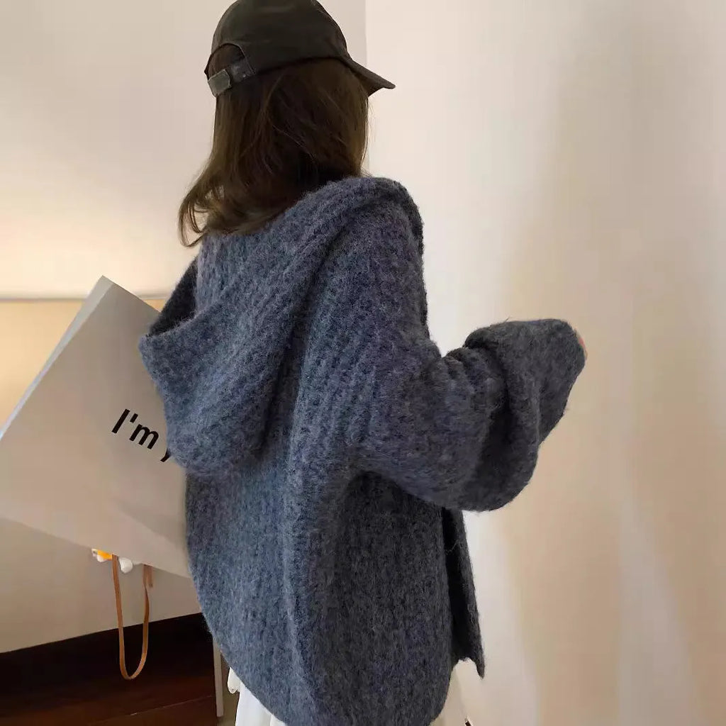 A woman wearing a thick, loose-fit, dark grey hooded sweater cardigan with a retro design.