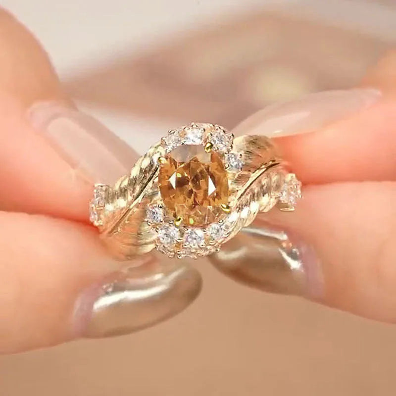 Gold-colour women's ring with an embossed feather design and a central yellow zircon stone on a finger.