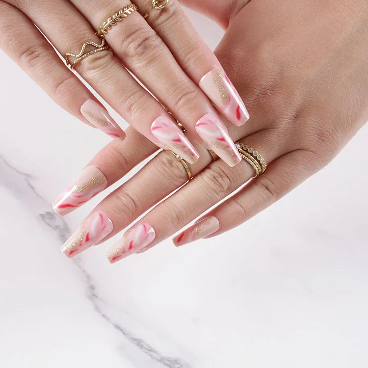 Set of pink press-on artificial nails with rose pattern, shown next to a bottle of nail glue.